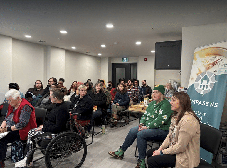 A roomful of co-op members at a meeting, with a Compass NS banner